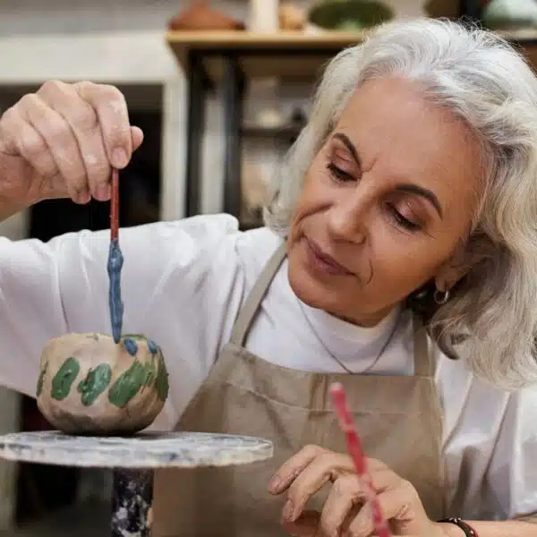 elder woman painting a pot for money