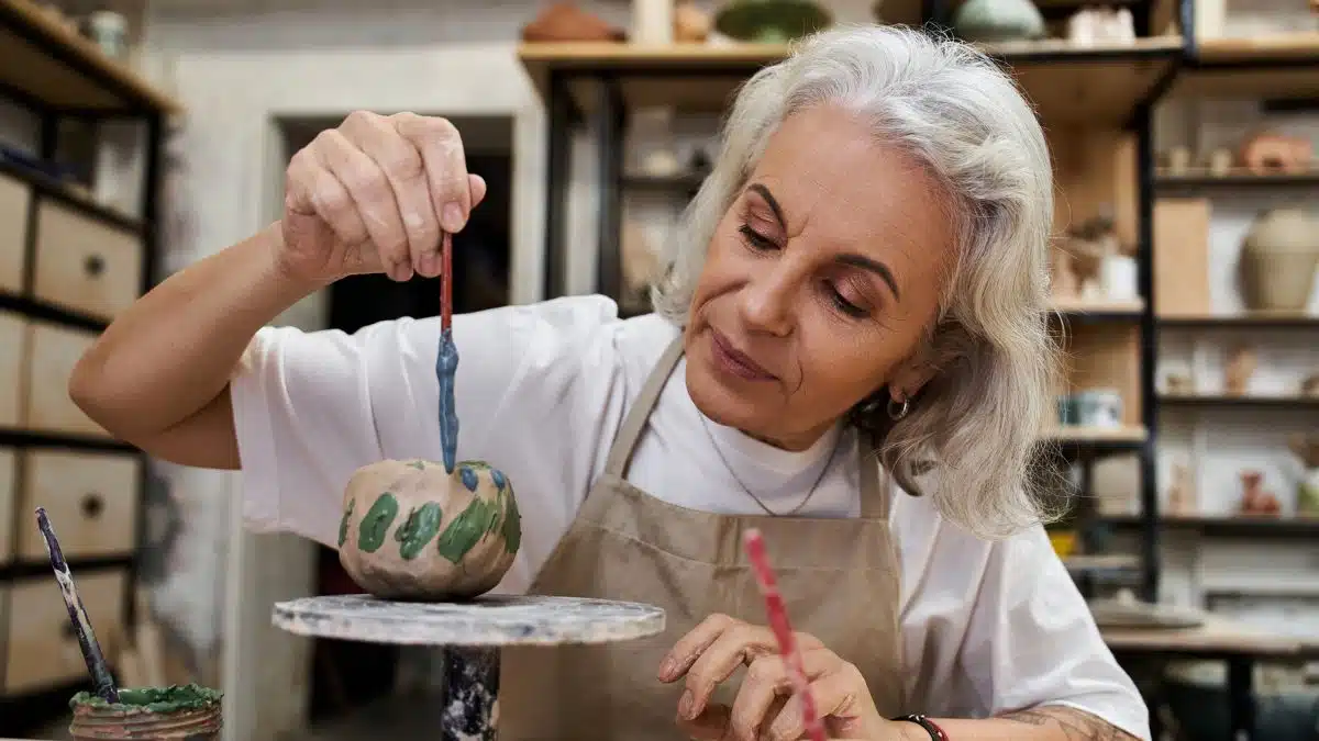 elder woman painting a pot for money